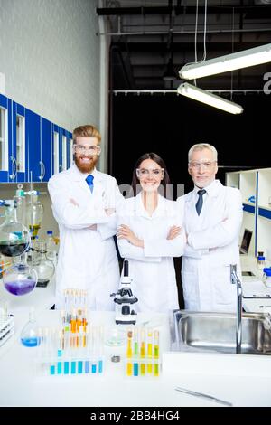 It`s a breakthrough! Successful group of three scientists are smiling, they finished an experiment in the lab, have great results, all are wearing Stock Photo
